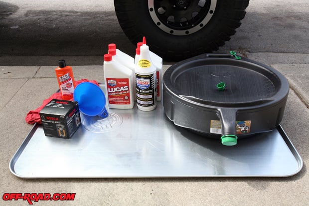 The basic supplies needed for an oil change can be found at any auto parts store. An oversized metal oil catch tray helps capture any oil spills, and the oil drain pan (like the plastic one shown) captures the oil and makes it easy to dispose of at the auto parts store. Aside from that, we have new Synthetic Lucas Oil (10W30 is recommended in our owners manual for our TJ Wrangler, though operating temperatures will dictate which viscosity to use), a new Bosch oil filter, and a funnel for pouring the oil. Having a few rags on hand is good for messes. Tip: Cat litter is very absorbent and can help quickly soak up spills. Dirt or sand will also suffice.