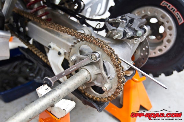 Starting on the left of the machine, we opted to install a sprocket guard to insure limited damage could occur to our chain or drive sprocket. We removed the left rear wheel and sat it aside. Our next task was to remove the four bolts holding on the rear sprocket and chain. 