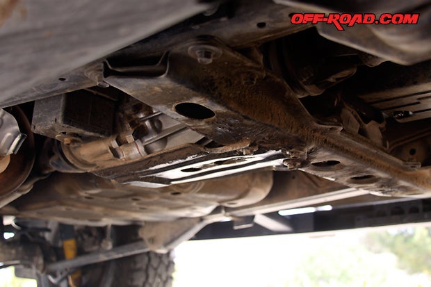 The factory transmission cross member is held in place by four bolts attached to the frame. From it stems a small and thin factory skid plate that offers minimal protection for the transfer case. Both will be replaced by Slee Off-Road Belly Pan.