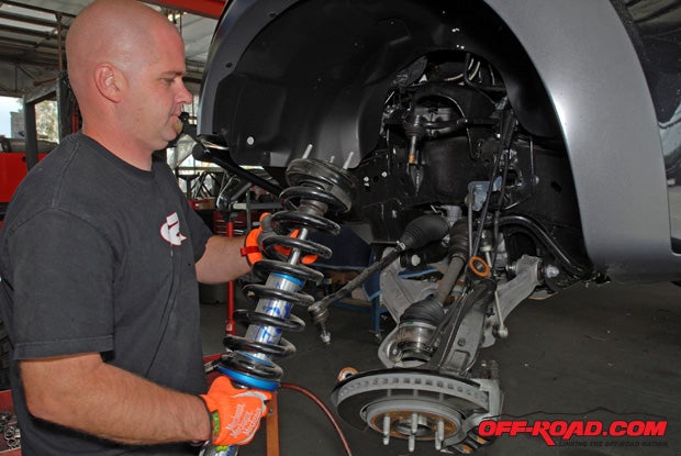 SoCal SuperTrucks technician Ryan Poe handled every aspect of the Raptor upgrade. Poe starts by using an impact gun to free the spindle from the upper A-arm. One smart strategy that Poe employs is to loosen the nut that holds the disc brake to the spindle, gaining a little more work space to access the lower shock mount.