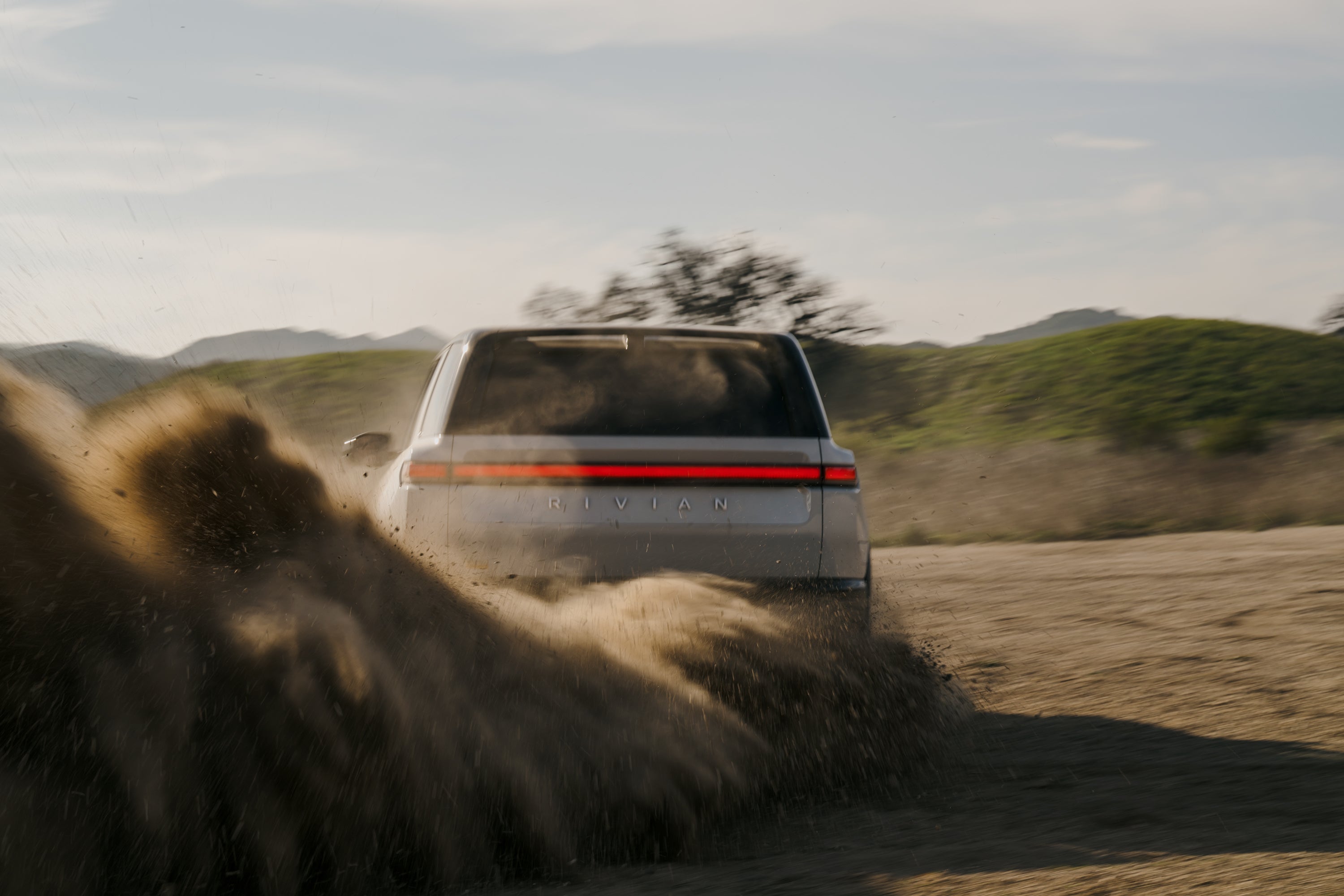 The new Rivian R2 is seen from the rear, sliding through dirt